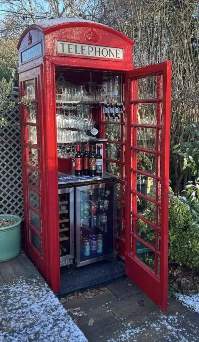 Red telephone booth repurposed as a mini bar with drinks and glasses inside.