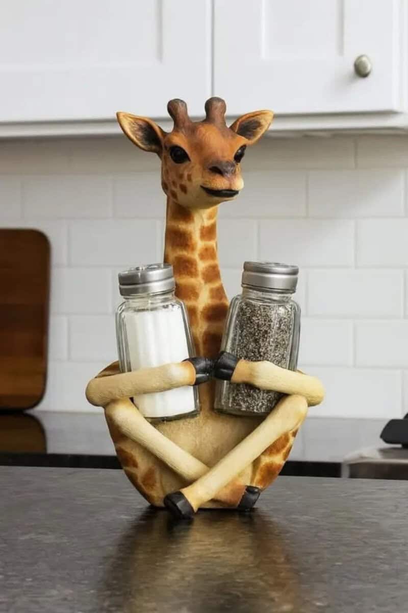 Giraffe-shaped salt and pepper shakers with arms holding them, on a kitchen counter.