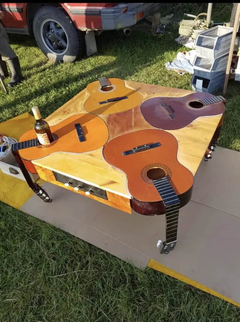 Multiple acoustic guitars and a bottle on a table outdoors.