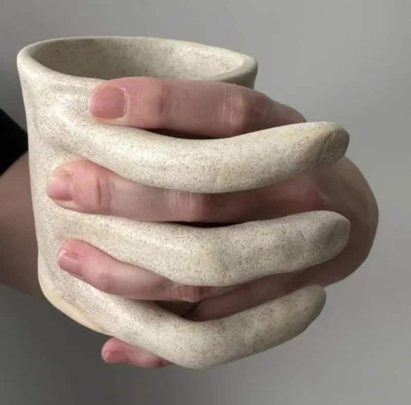 Hand holding a ceramic cup with a unique, elongated finger-like handle design.