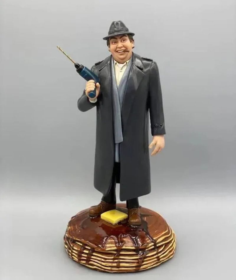 Figurine of a man in a coat and hat holding a drill, standing on a stack of pancakes.