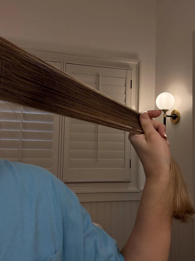 Person holding a long strand of blonde hair in front of a wall with a lamp.