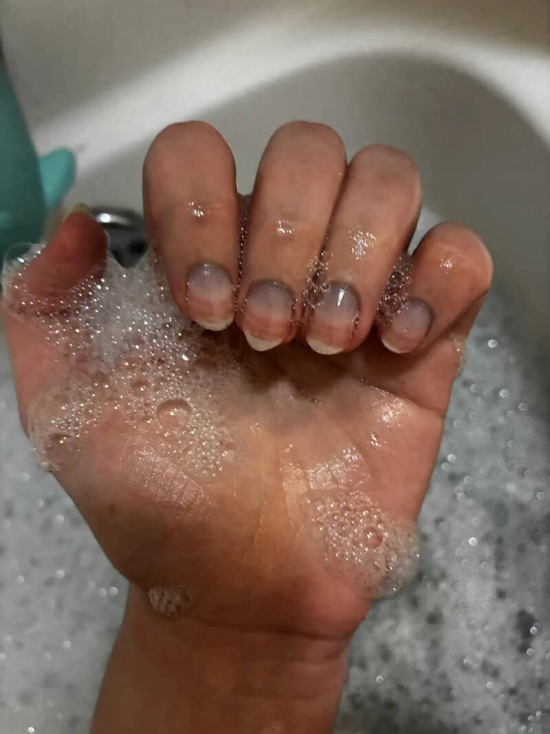 Close-up of a hand with soapy bubbles, fingers curled inward, in a bath.