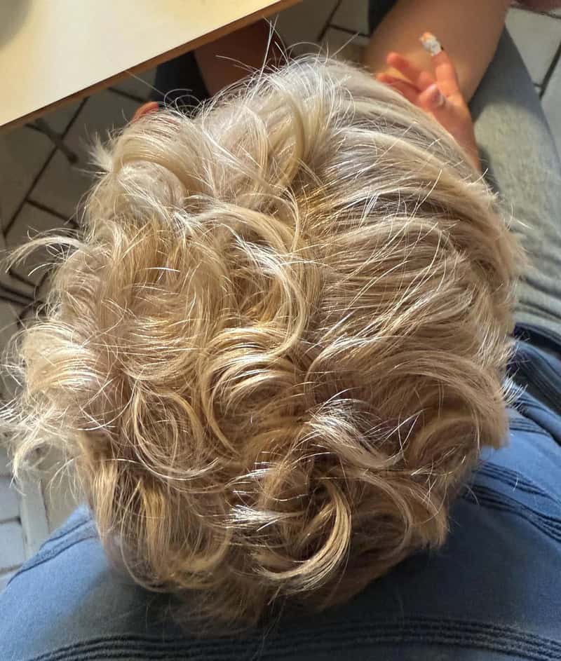 Close-up of a person's curly blonde hair from above.