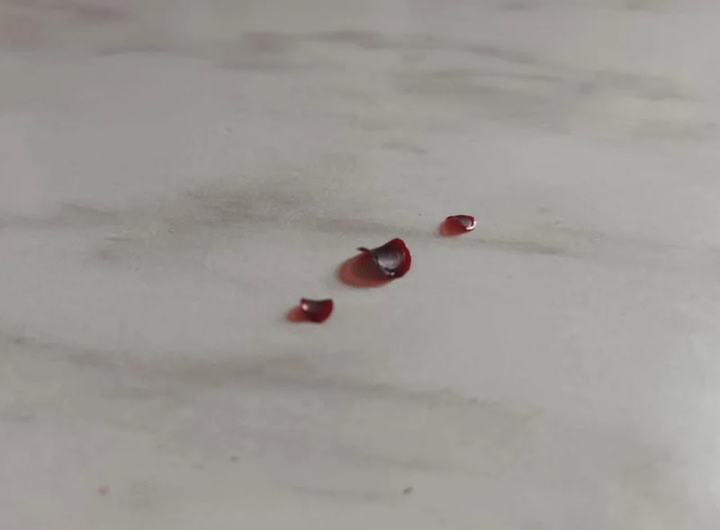 Three small red blood droplets on a light surface.