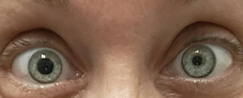 Close-up of a person's wide-open green eyes with visible eyelashes and eyebrows.