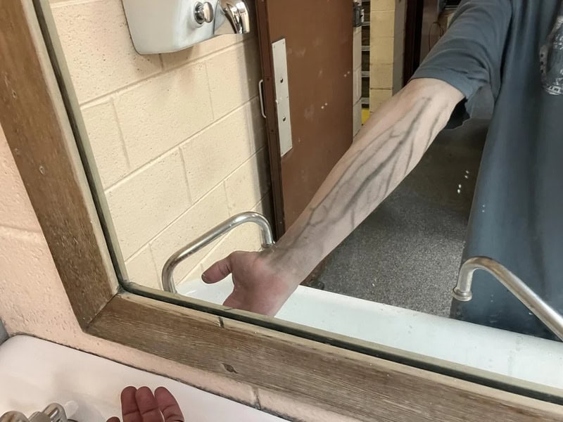 Person with tattooed arm reaching into a mirror, showing part of their body.