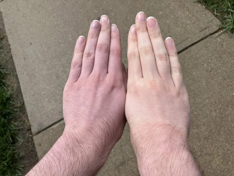 Two hands with different skin tones held side by side on a sidewalk.