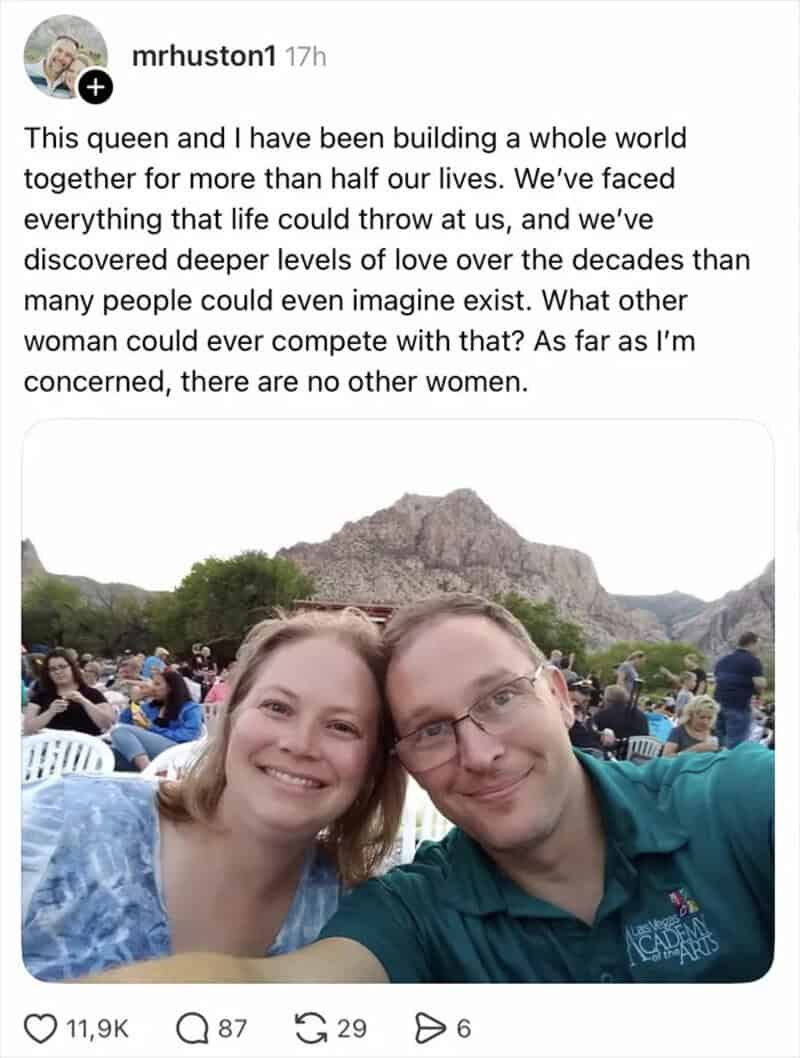 A smiling couple taking a selfie outdoors with mountains in the background.