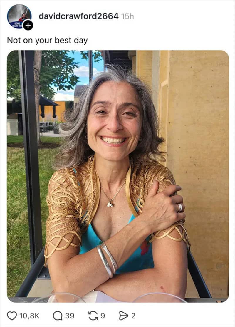 Smiling woman with gray hair, wearing a blue top and gold shawl, sitting outdoors.