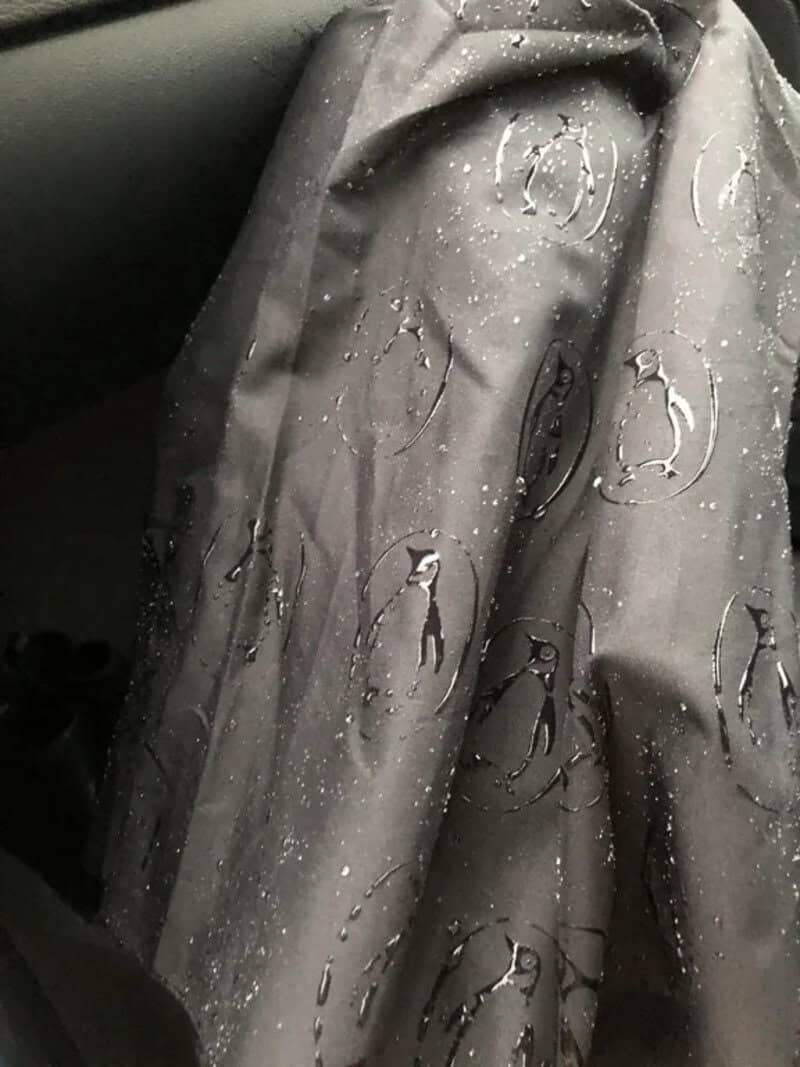 Rain-soaked gray raincoat with penguin pattern and water droplets.