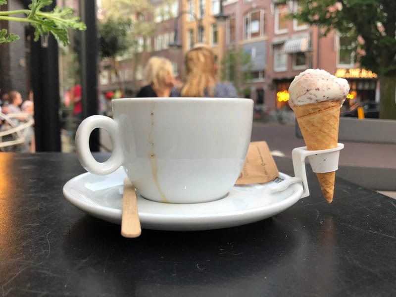 Coffee cup with an ice cream cone attached to the side, on a black table outdoors.