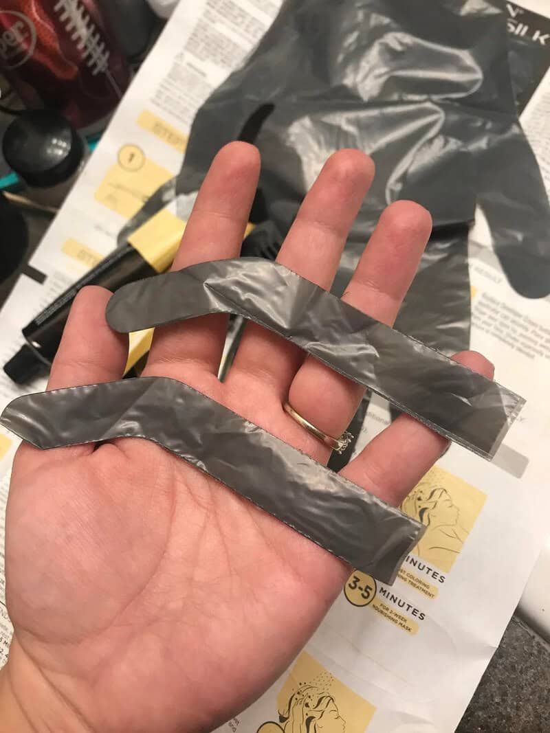 Hand holding two gray plastic strips with a black cable in the background.