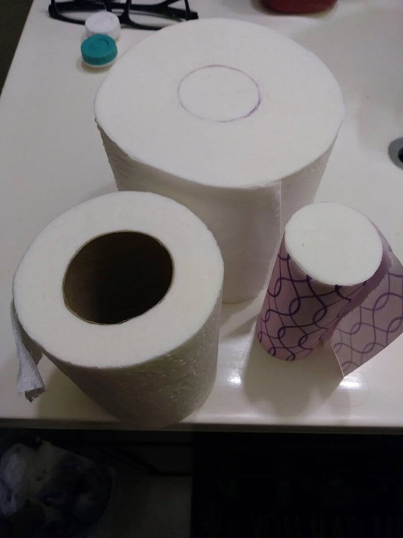 Three toilet paper rolls with one unwrapped and one with a purple pattern.