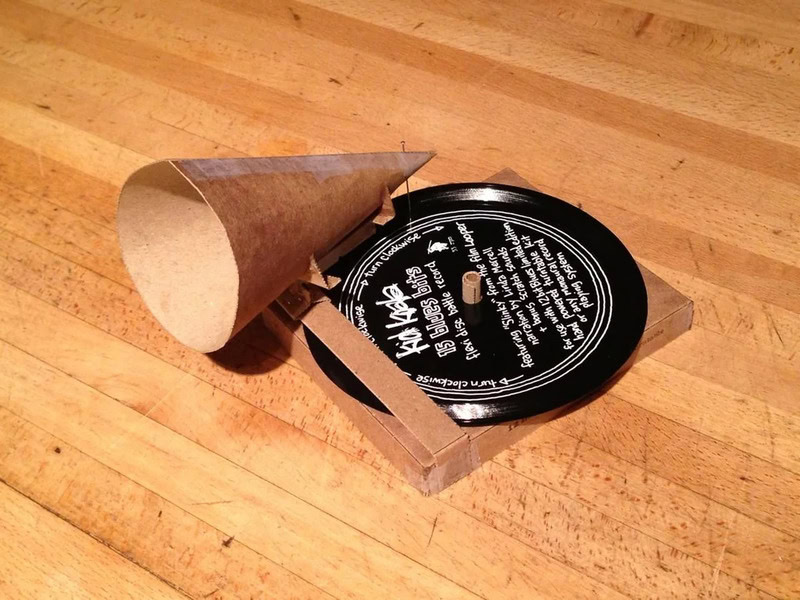 A cardboard coffee cup holder with a black plastic lid on a wooden surface.