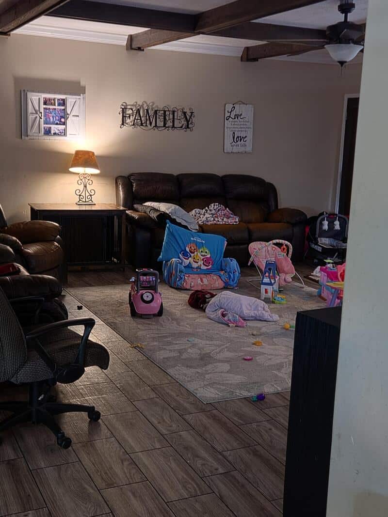 Living room with toys scattered on the floor, a sofa, and wall decor reading 'FAMILY' and 'Love'.