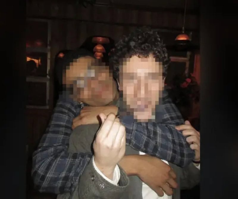 Two people hugging, one making a finger heart gesture, faces pixelated.