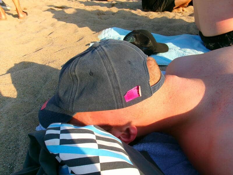 Person lying on beach with a cap and striped shirt, sunbathing on sand.