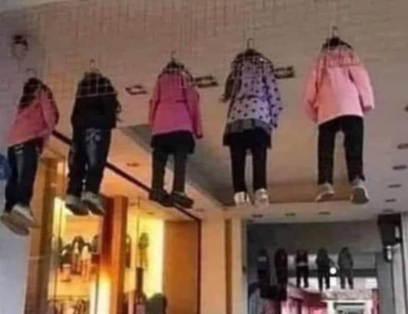 Five people appear to be hanging upside down from the ceiling in a mall.