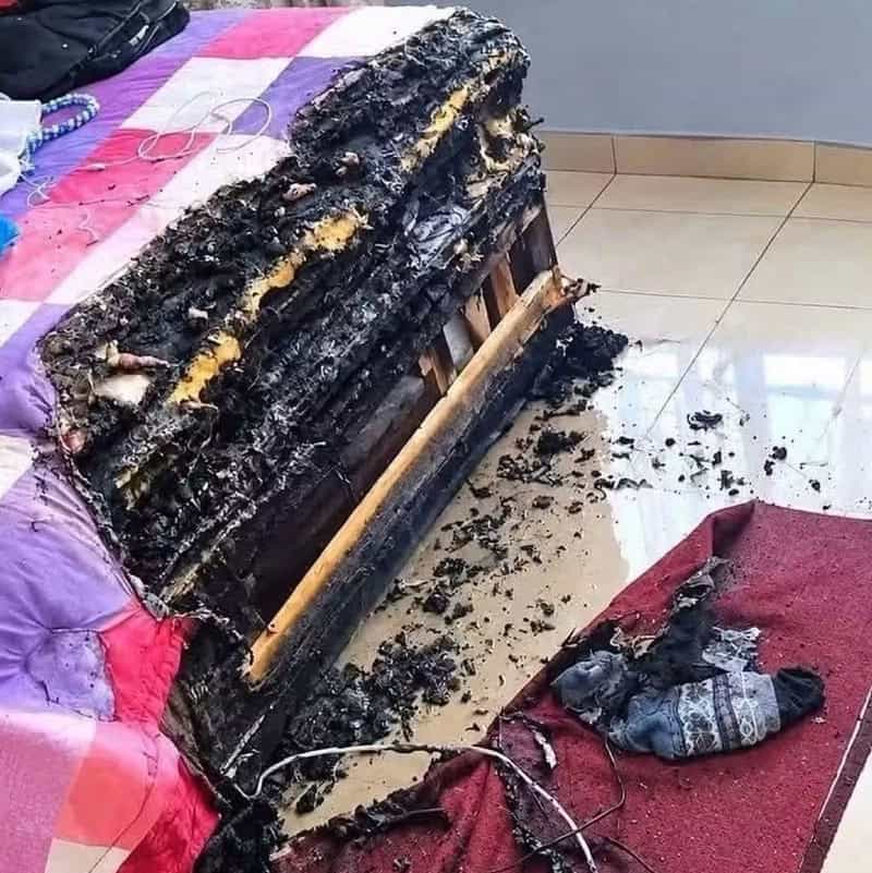 Burned mattress with charred remains and melted fabric on a tiled floor.