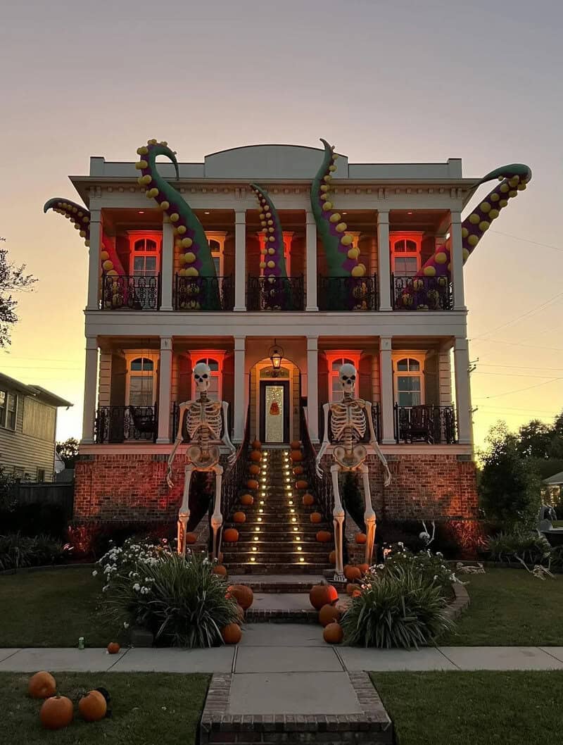 Two-story house decorated with skeletons on stairs and colorful balloons; pumpkins line the walkway,.