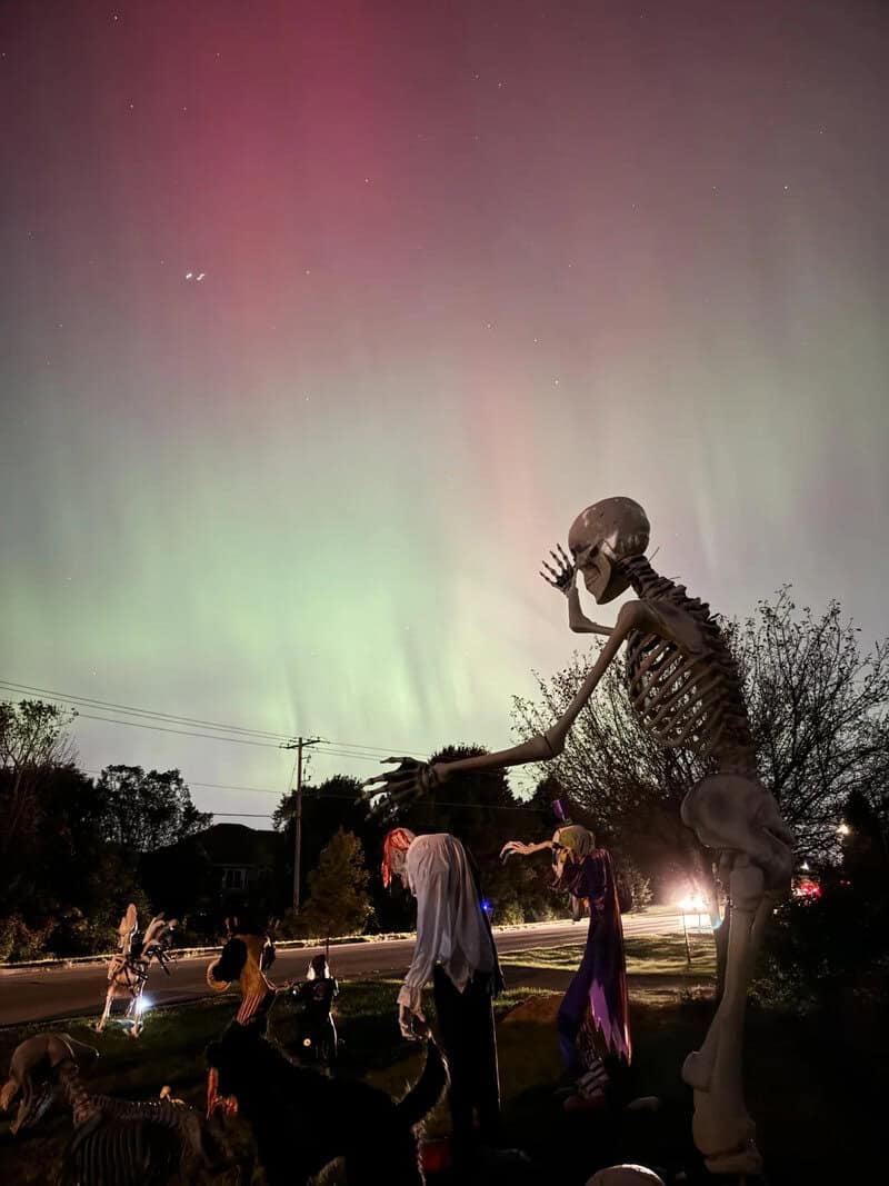 A Halloween scene with a large skeletal figure leaning over a group of people at night, orange and t.
