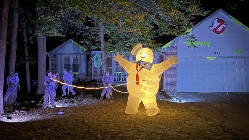 Animated light-up skeletons and a large inflatable yellow figure with red tie in front of a suburban.