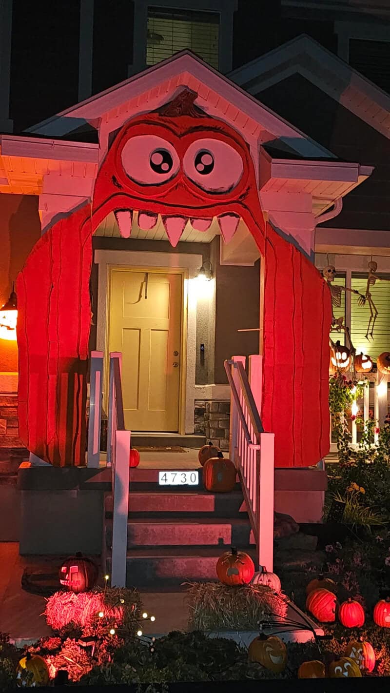 Halloween-themed porch with a red inflatable monster arch over the front door, steps, pumpkins, and:.