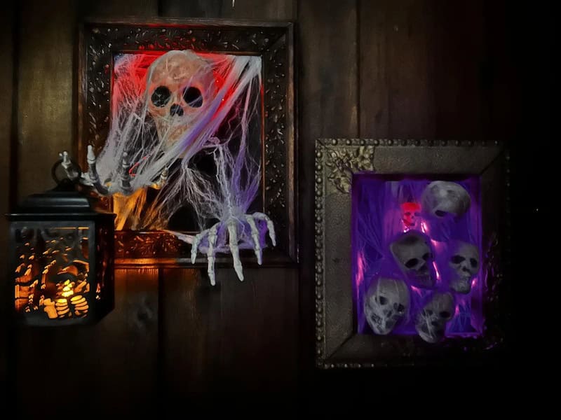 Decorative Halloween scene with framed skulls in cobwebs and purple and orange lighting.