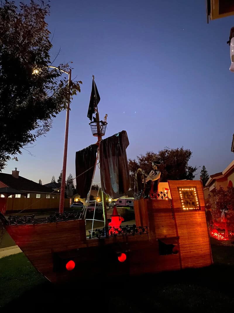 Halloween-themed outdoor setup at dusk with a wooden stage, red lighting, a flag, and decorative lit.
