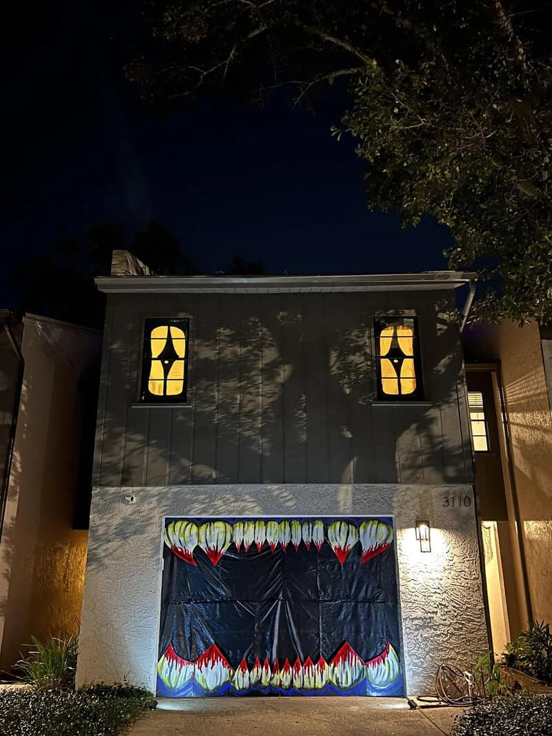 Two-story suburban house at night with lit windows and a garage door decorated with a jagged, multih.