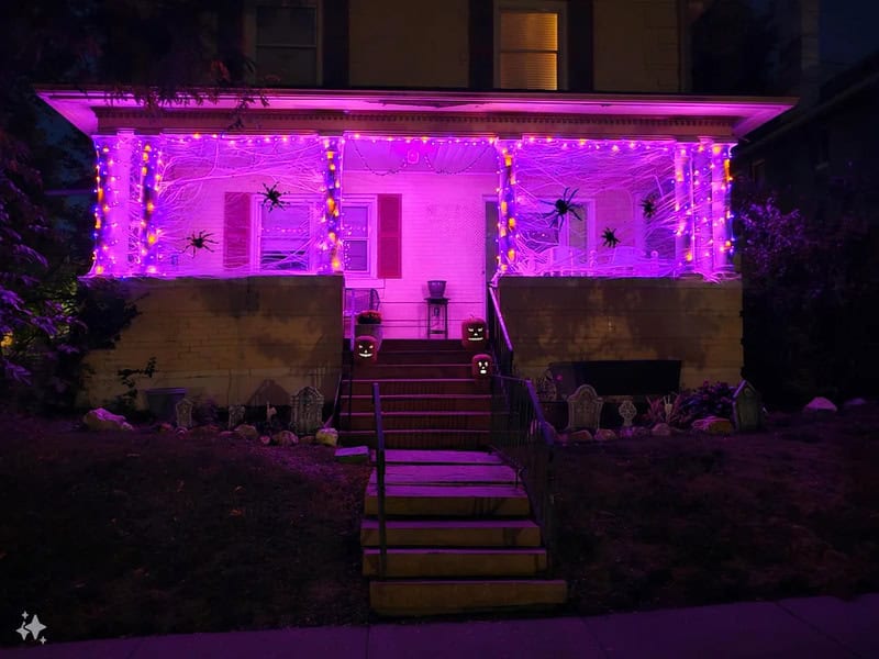 House exterior lit with purple Halloween lights and decorations on porch, steps leading to entrance,.