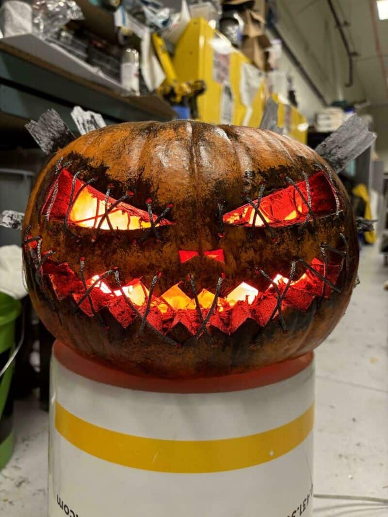 Lit jack-o'-lantern pumpkin with glowing carved face on a workshop shelf, Halloween.