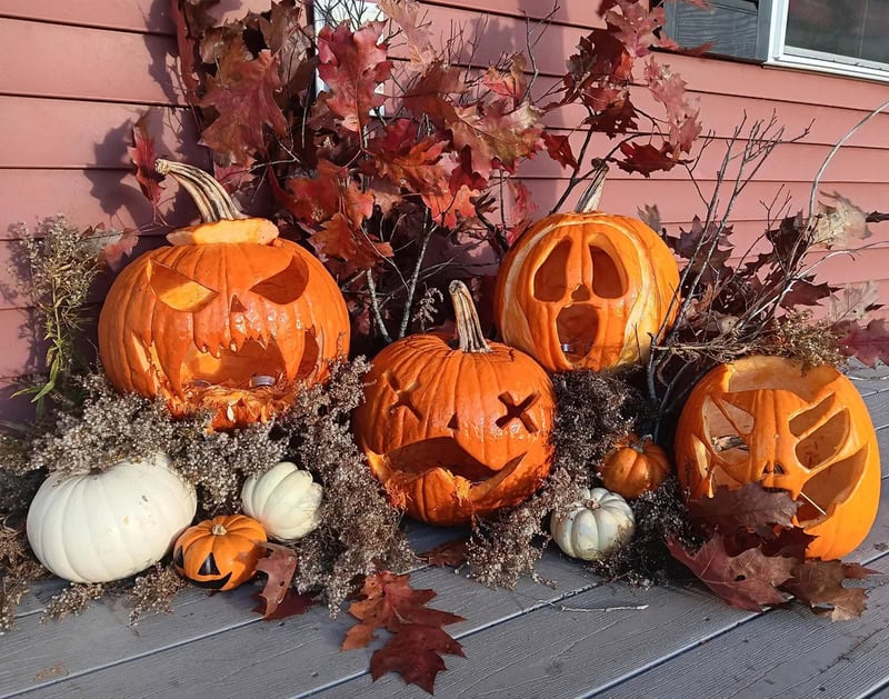 Row of carved pumpkins with autumn leaves against a house wall, Halloween décor.