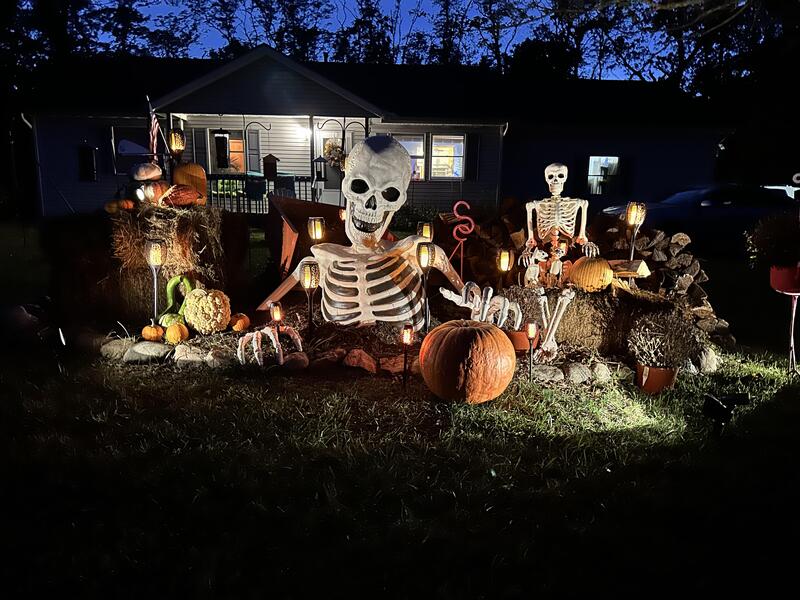 Halloween yard with illuminated skeletons, pumpkins, and festive decorations in front of a house at夜.