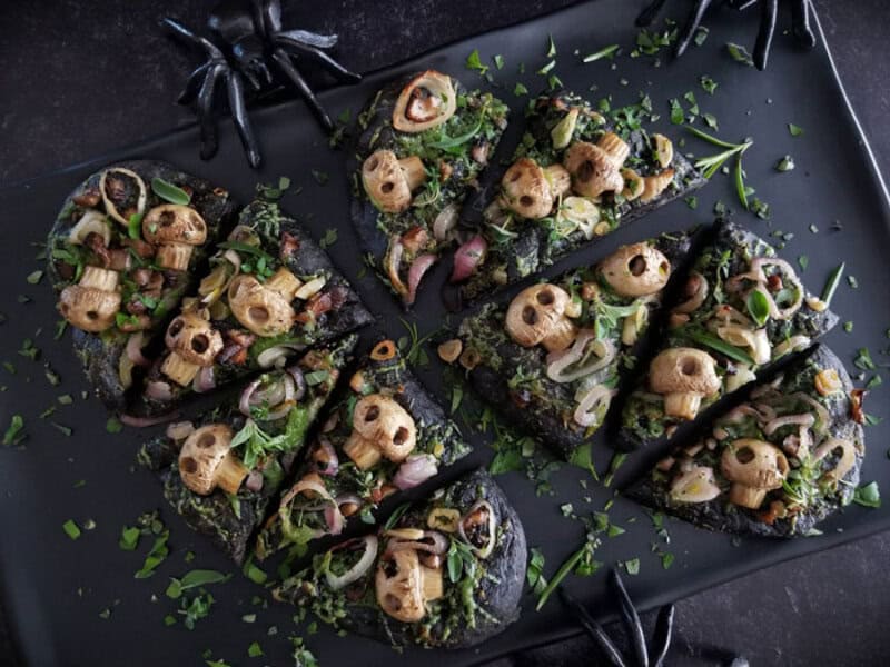 Spooky Halloween food ideas: black squid ink toasts topped with greens, onions, and Halloween-themed.