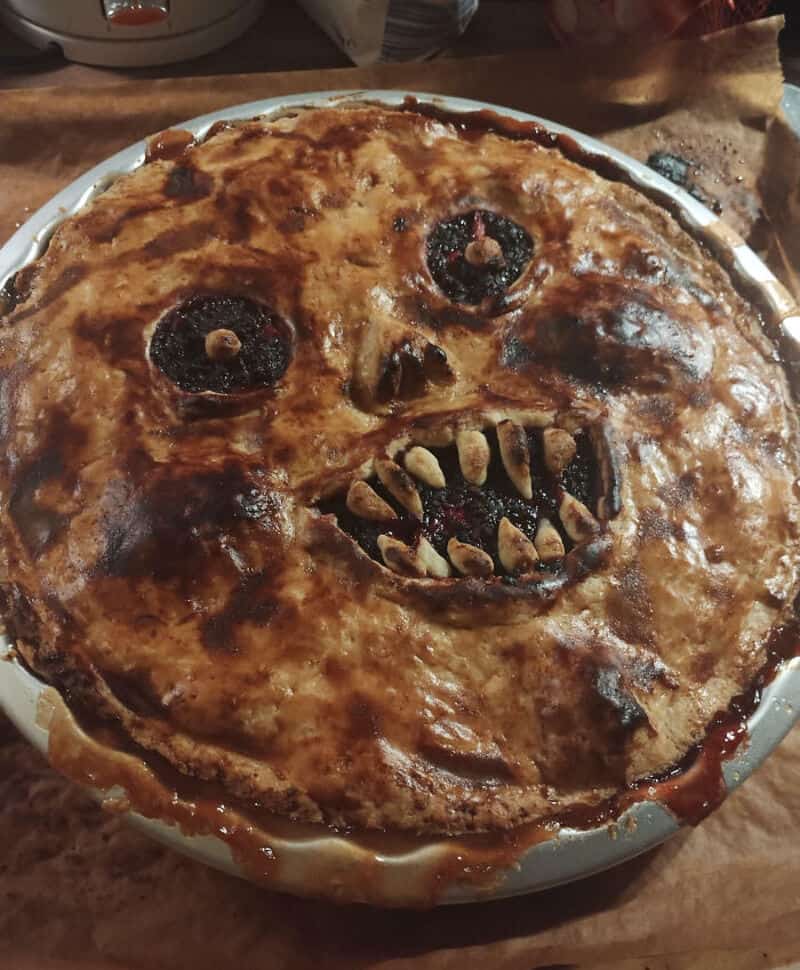 Spooky Halloween pie with a face, burnt crust, hollow eyes and jagged teeth in a baking dish.