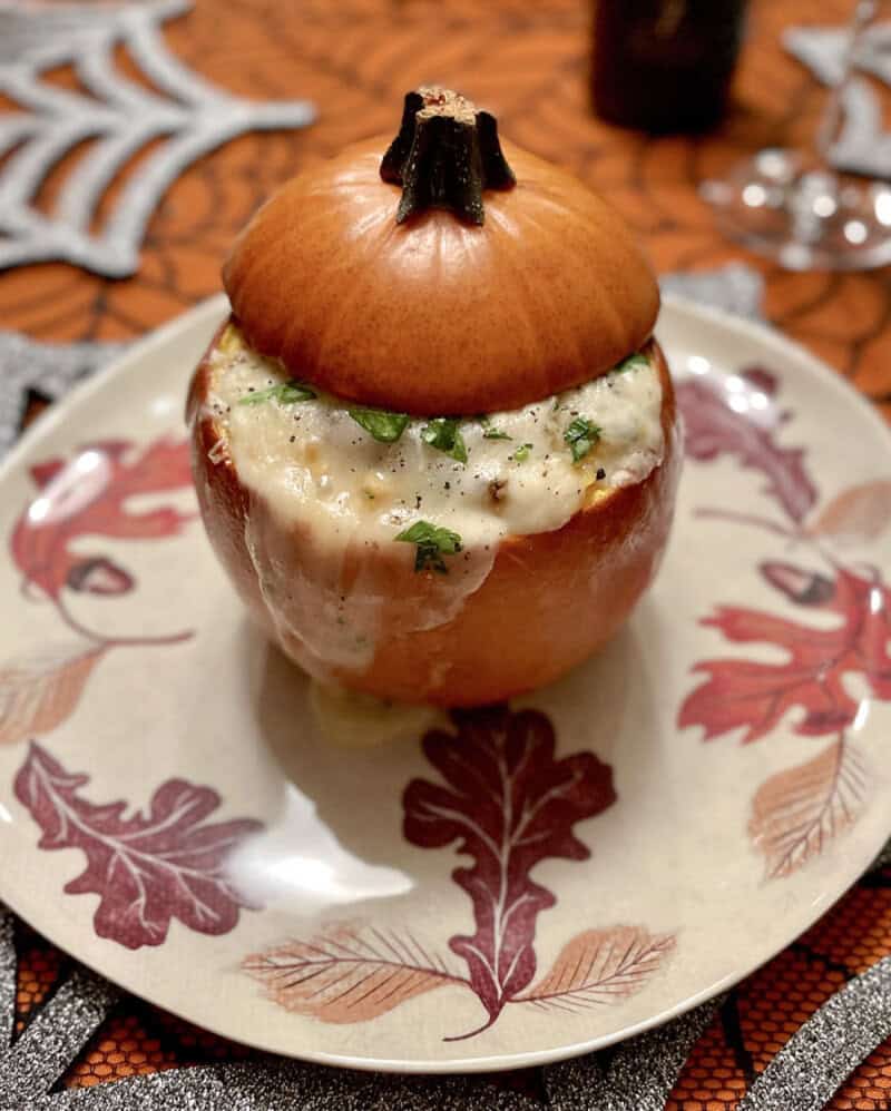 Stuffed mini pumpkin with creamy herb filling, on a decorative plate with autumn leaves.