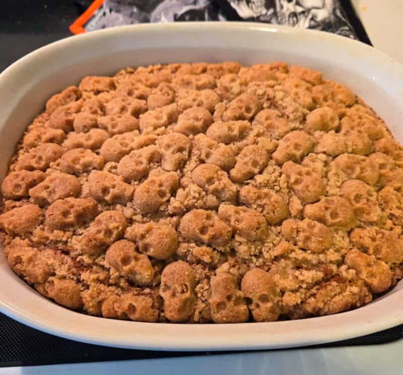 Mini pumpkin-colored cookies arranged in a crumbly topping in a white baking dish for spooky treats.