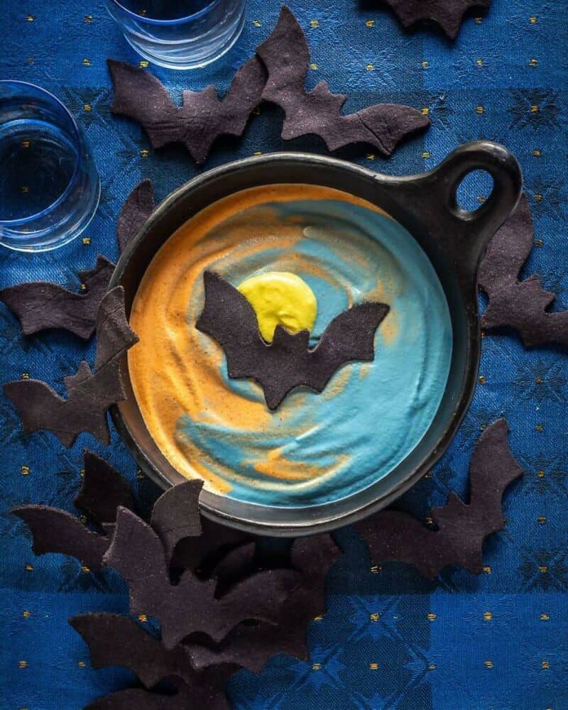 Bat-shaped chocolate decorations on a colorful swirl frosting in a small black skillet, spooky blue,.
