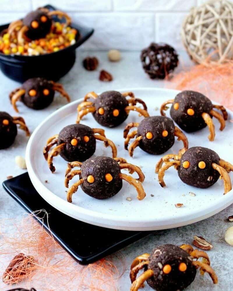 Spooky Halloween spider treats: chocolate peanut butter balls with pretzel legs on a white plate.
