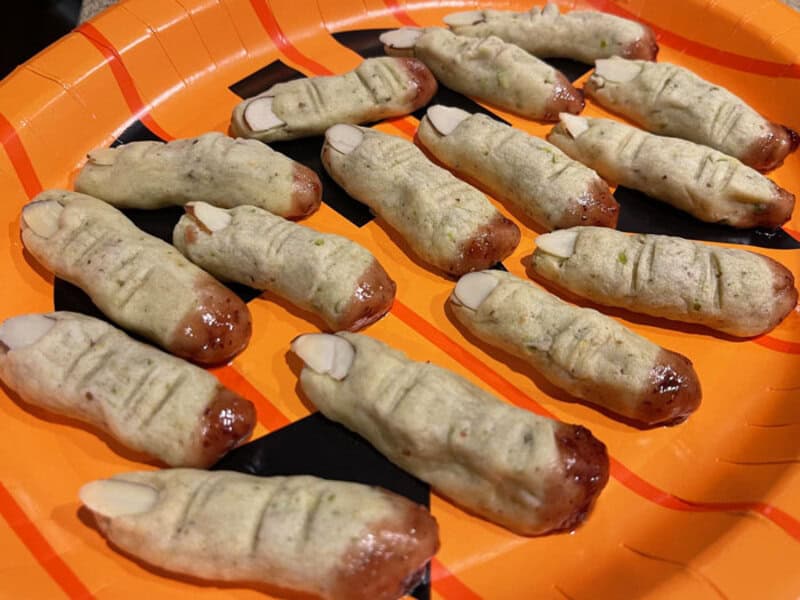 Mini sausages wrapped in pale dough on an orange platter; some have small slits.