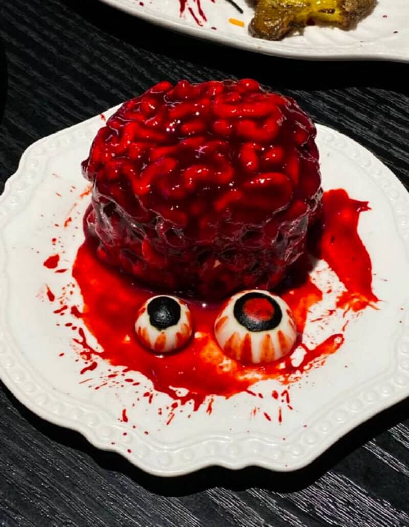Spooky red brain dessert with two candy eyeballs on a white plate.