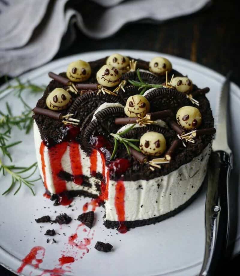 Halloween-themed Oreo cake with chocolate drizzle, white cream, red sponge interior, and candy eyebl.
