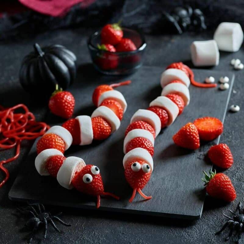 Strawberry pinwheel skewers with alternating white chocolate slices on a dark board, decorated for a.