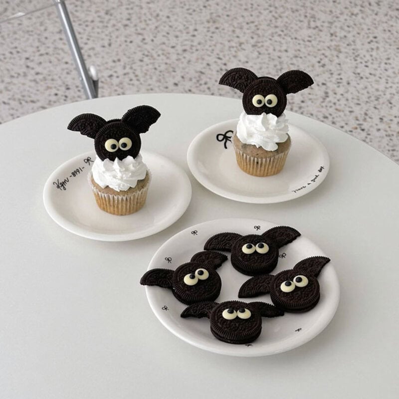 Halloween bat-themed cupcakes and cookies arranged on white plates.