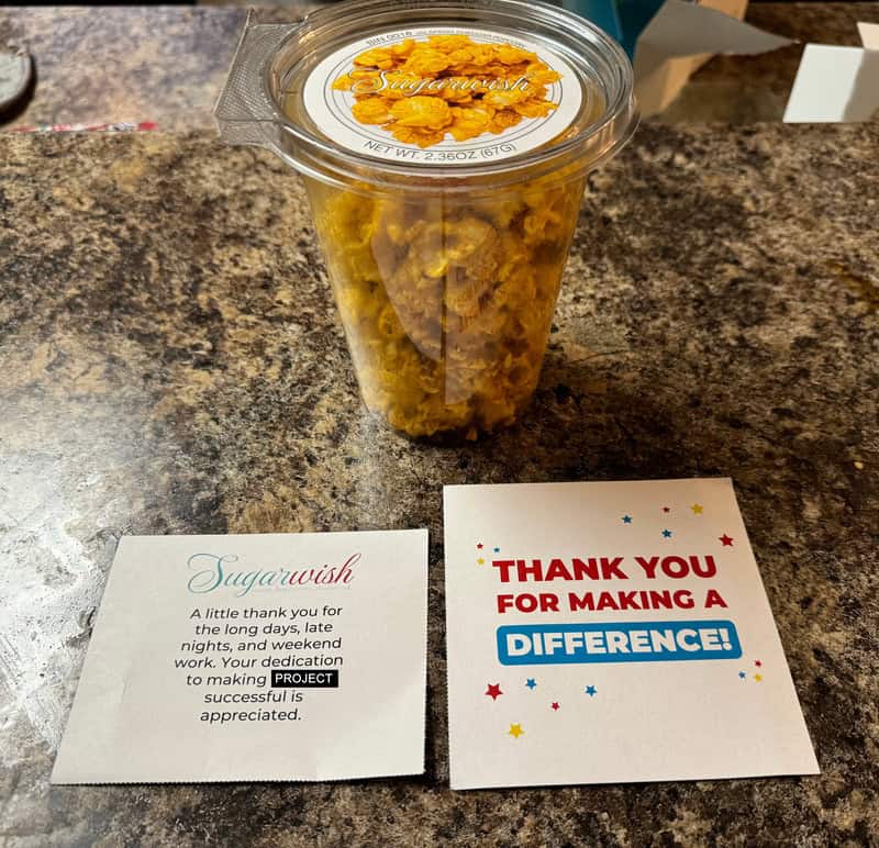 Container of popcorn with a thank you card and a note from Sugarwish on a countertop.