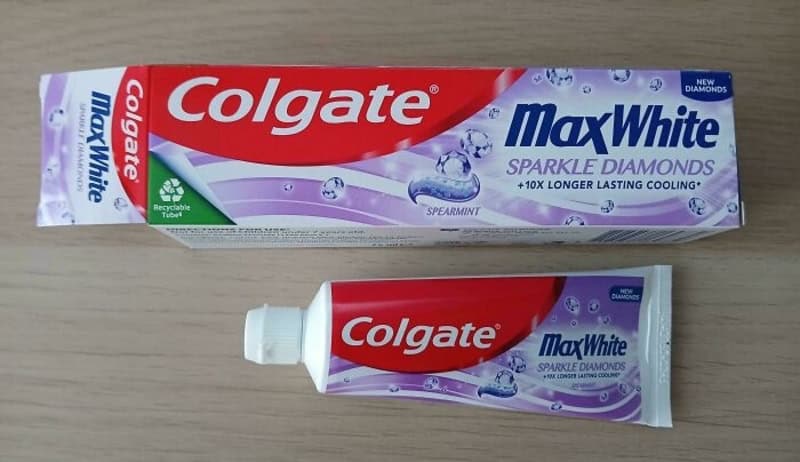 Colgate MaxWhite toothpaste with sparkle diamonds packaging and tube on wooden surface.