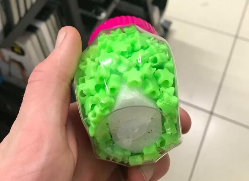 Small hand holding a green crinkle-shape toy with a pink cap.