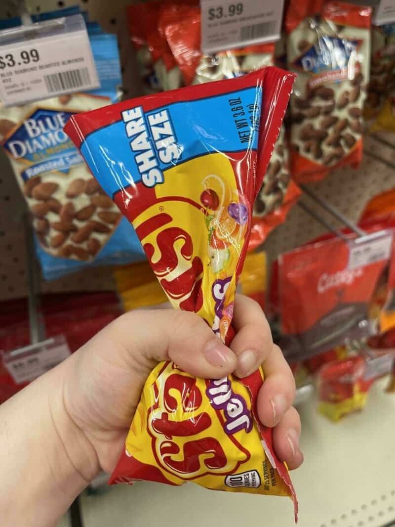 Person holding a Snack Pack candy in a store aisle with other snacks on the shelves.